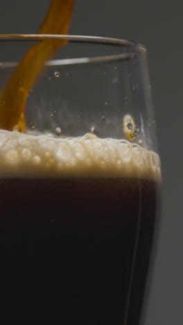 Vertikales-Video-Nahaufnahme-Von-Irish-Stout,-Das-In-Glas-Vor-Schwarzem-Studiohintergrund-Gegossen-Wird,-Um-Den-1.-Tag-Von-St.-Patricks-Zu-Feiern